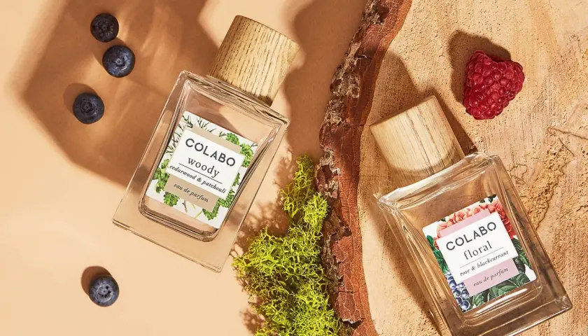 Dwa flakony perfum COLABO: "woody" z jagodami i "floral" z maliną, otoczone mchem i drewnem.