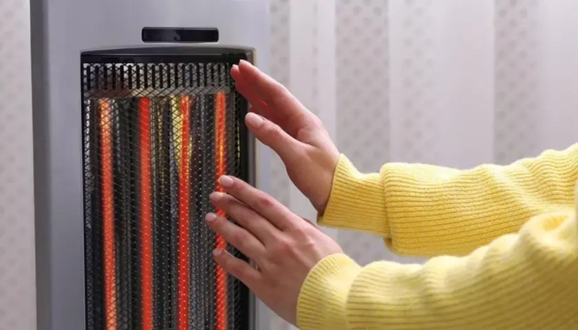 Manos cerca de un calentador eléctrico encendido. Las estufas eléctricas son peligrosas, ¡mantén la distancia!