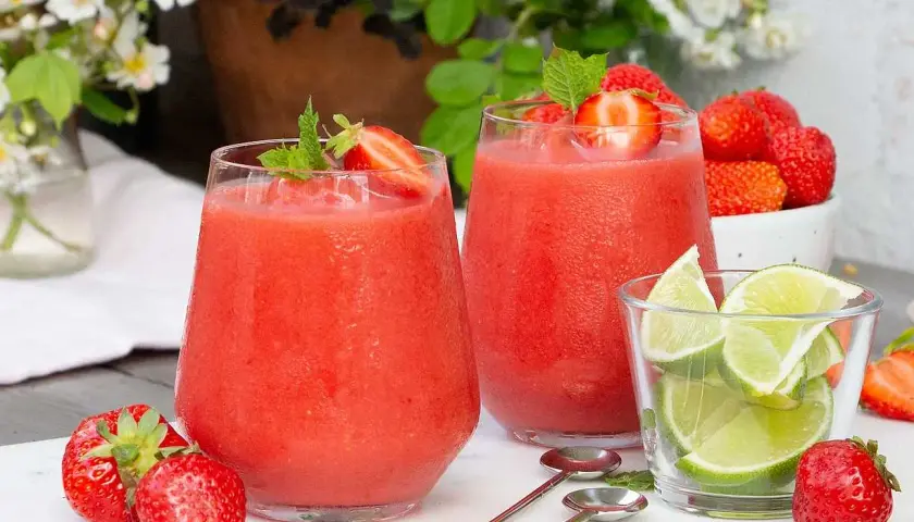 Två frostiga jordgubbsdaiquiri-drinkar med mynta och jordgubbar, serverade med limeklyftor och färska jordgubbar.