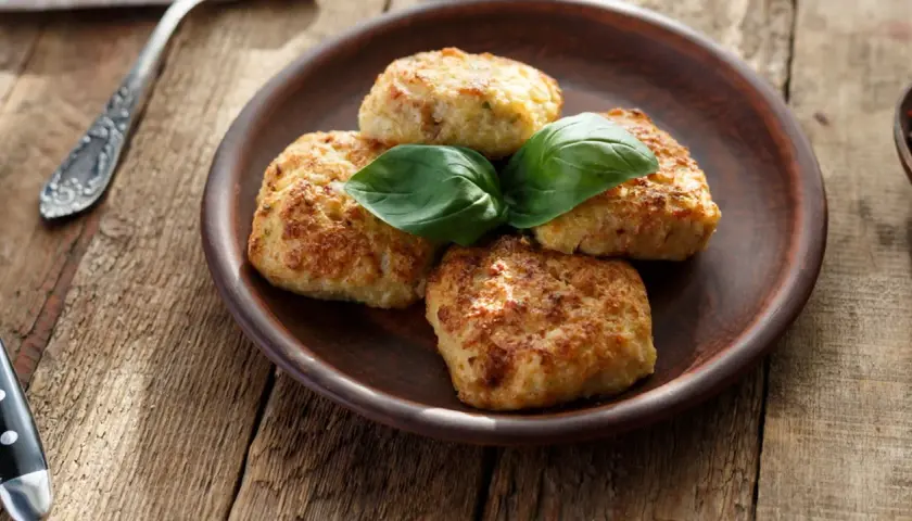 Quattro polpette di zucchine e patate dorate, guarnite con basilico fresco, su un piatto di terracotta.
