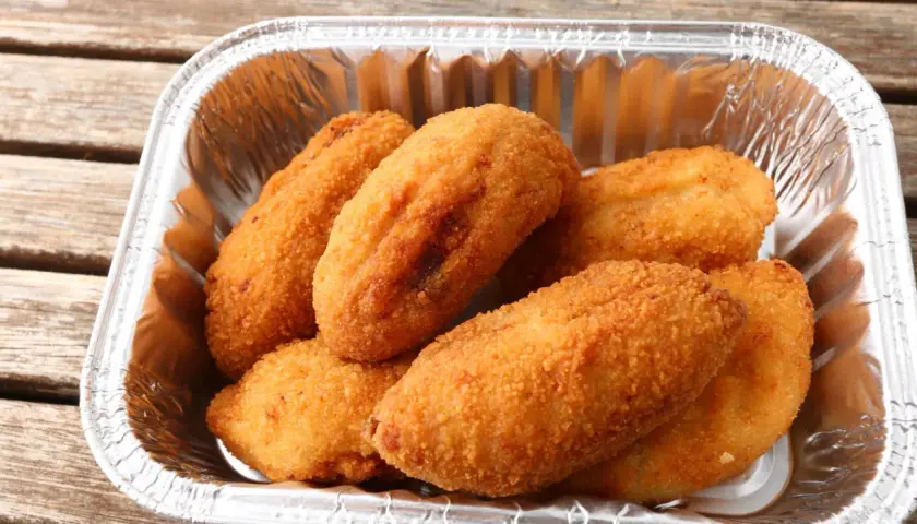 Croquetas de pollo doradas y crujientes en un recipiente de aluminio, listas para disfrutar.