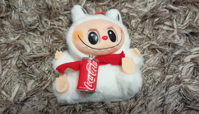 Pluszowy stworek z czerwoną szalikiem i puszką Coca-Coli, jakby to była największa zabawka na świecie.