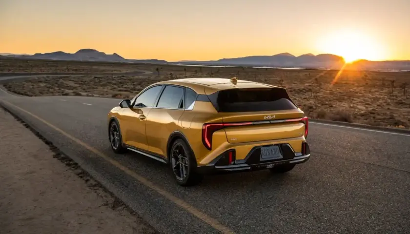 Un coche hatchback amarillo brillante recorre una carretera desierta al atardecer, con las montañas al fondo.