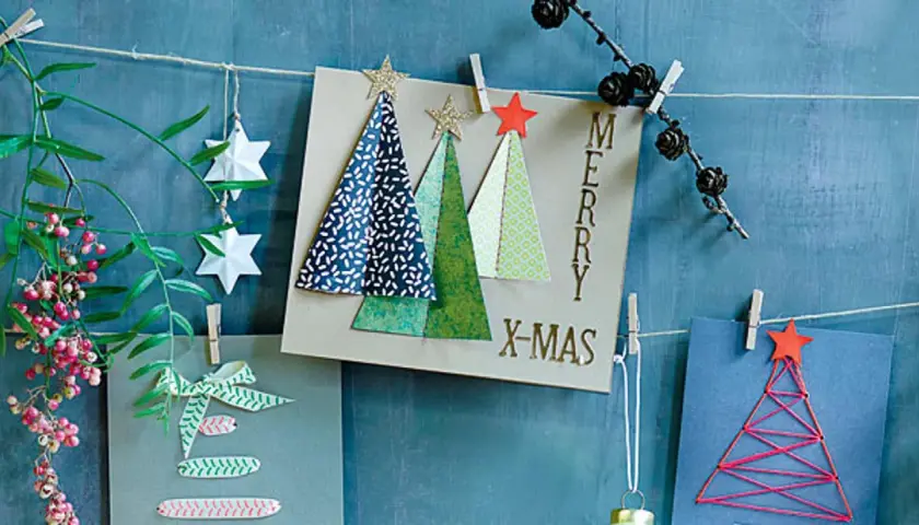 Moderne weihnachtskarten basteln: Karten mit Bäumen, Sternen und Schriftzug "Merry X-Mas" hängen an einer Schnur.
