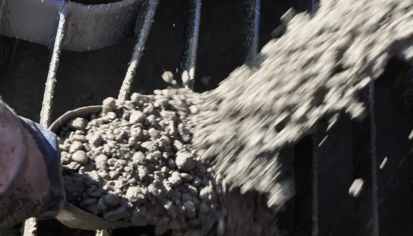 Beton wird mit einer Schaufel durch ein Gitter gegossen, das den Anforderungen der DIN EN 196-1 entspricht.