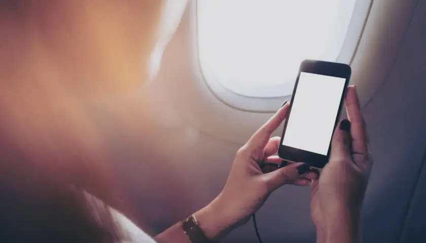 Ręce trzymające smartfon z pustym ekranem, siedząc przy oknie samolotu. Zastanawiasz się, czy bez karty SIM można dzwonić?