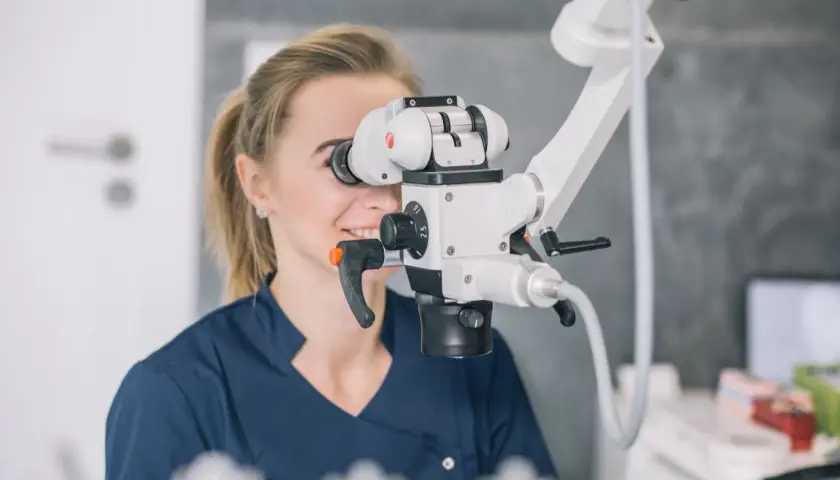 Dentystka wykonuje leczenie kanałowe pod mikroskopem, precyzyjnie pracując z użyciem nowoczesnego sprzętu.
