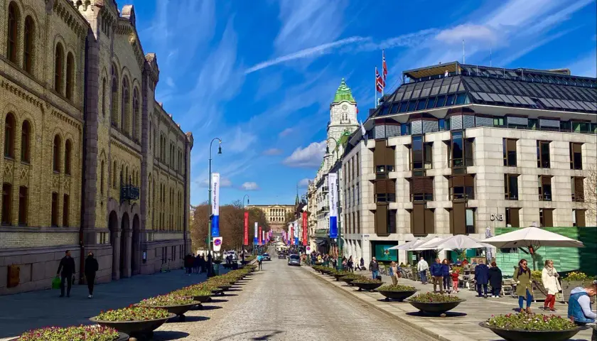 Słoneczny dzień na Karl Johans gate w Oslo. Brukowana ulica z rzędami kwietników prowadzi do Pałacu Królewskiego.