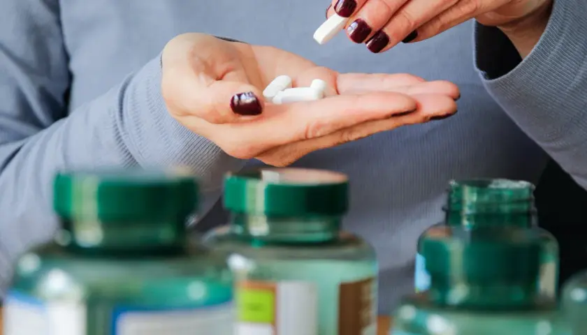 Frau nimmt weiße Kapseln aus der Hand, um die 5-HTP-Wirkung zu erfahren.