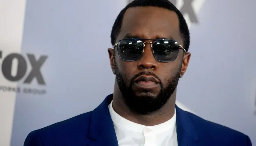 P Diddy w okularach przeciwsłonecznych i niebieskiej marynarce, z logo FOX w tle.