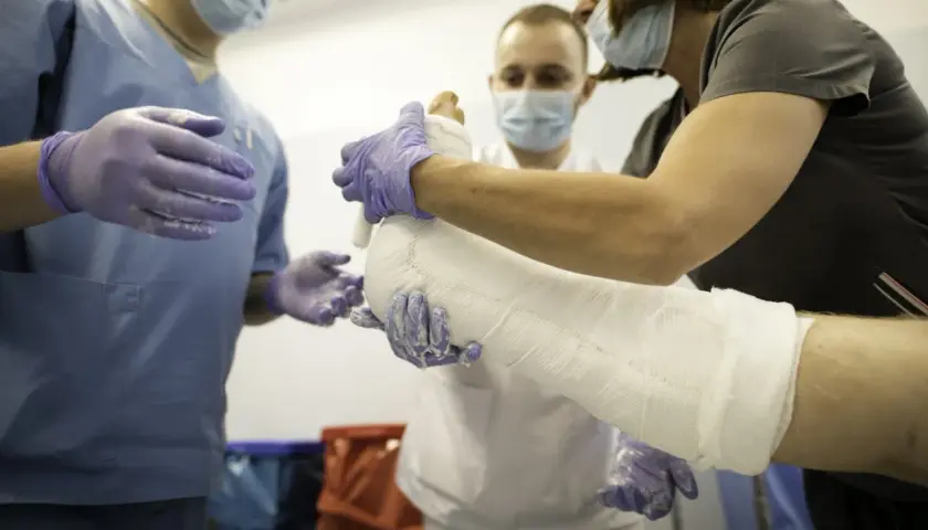 Trzech lekarzy w maseczkach i rękawiczkach zakłada gips na nogę pacjenta.