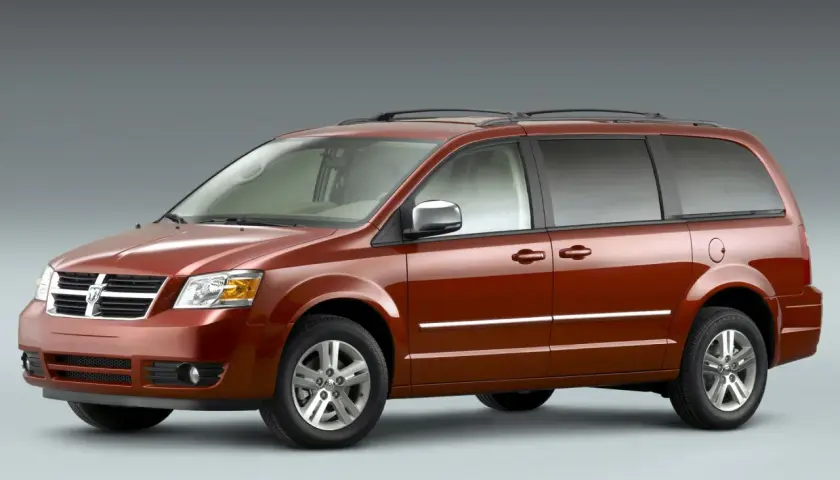 Pomarańczowy Dodge Grand Caravan z chromowanymi listwami i relingami dachowymi, gotowy na rodzinną podróż.