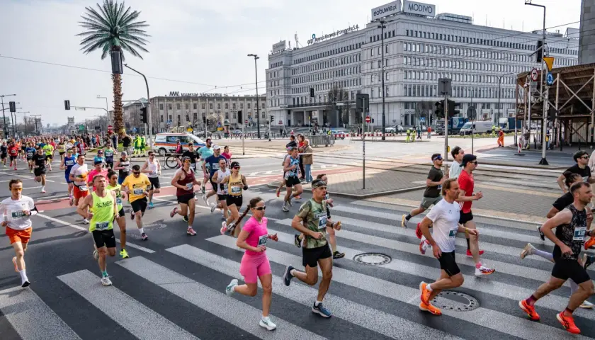 Uczestnicy biegu na ulicach Warszawy, biegacze przekraczają pasy. Biegi Polska to emocje i sport.