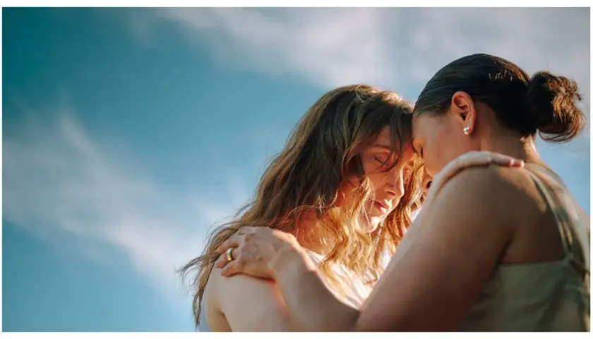 Due donne si abbracciano con dolcezza, un'immagine che evoca il vero amore platonico, significato di profonda connessione spirituale sotto un cielo azzurro.