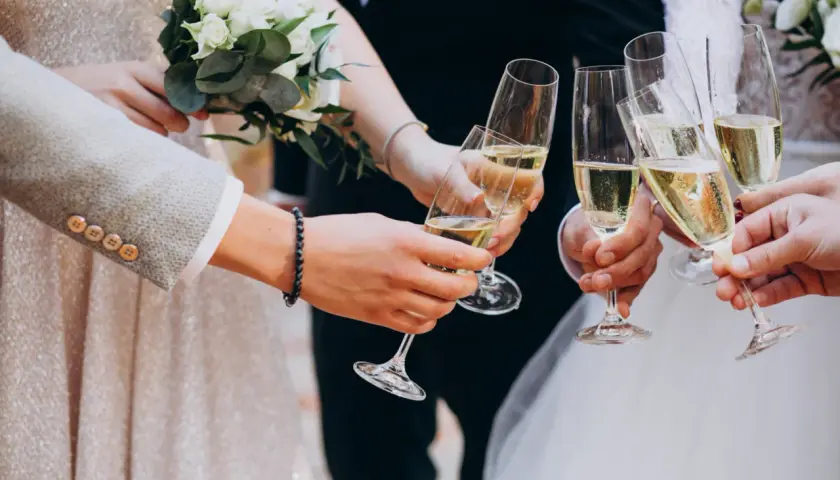 Para młoda i goście wznoszą toast kieliszkami szampana. Wino na wesele to symbol radości i celebracji.