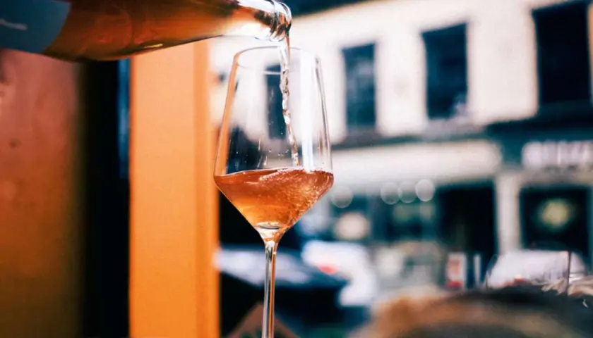 En flaska häller upp ett bubbligt, roséfärgat pet nat i ett elegant glas. En härlig kväll väntar.