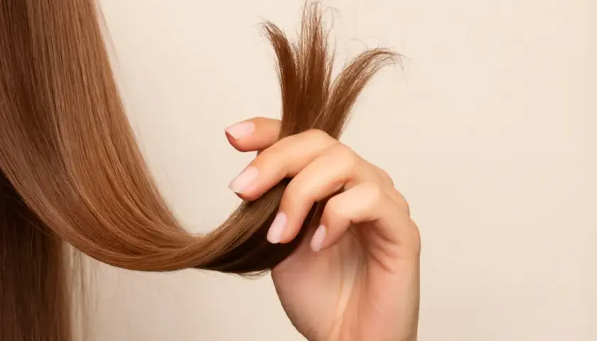 Mano sujetando mechón de cabello castaño con puntas abiertas, mostrando la necesidad de saber como reparar puntas abiertas para un cabello sano.