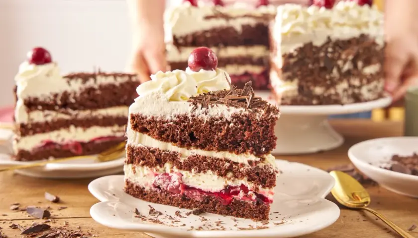 Pyszny tort szwarcwaldzki z mascarpone, przełożony kremem i wiśniami, ozdobiony czekoladowymi wiórkami i wisienką.