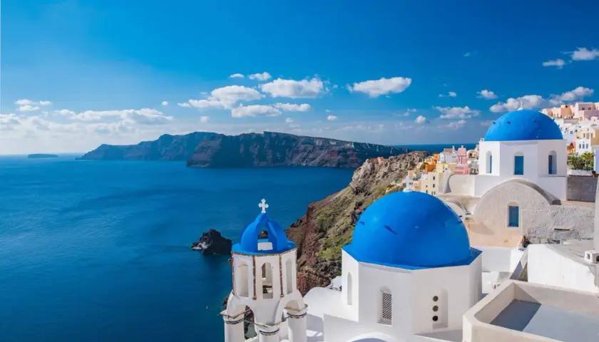 Santorini, idealne miejsce na wakacje w listopadzie gdzie najcieplej. Białe domy z niebieskimi kopułami nad lazurowym morzem.