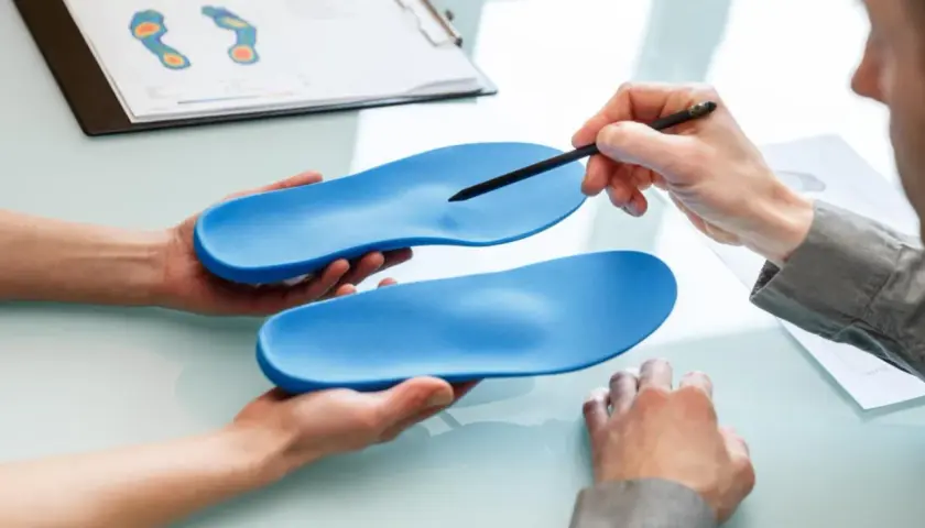 Beratung zu orthopädische einlagen kostenübernahme. Hände halten blaue Einlagen, ein Stift zeigt auf eine. Fußdruckanalyse im Hintergrund.