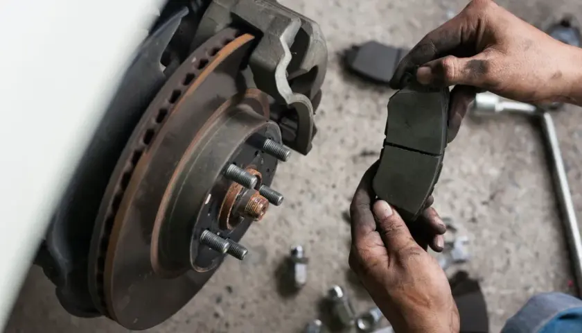 Mechanik trzyma nowe klocki hamulcowe, gotowe do wymiany przy zużytym hamulcu tarczowym.