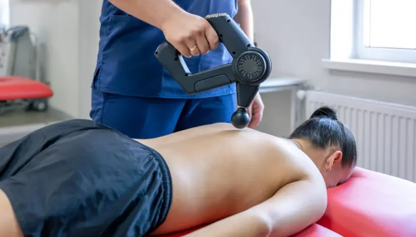 Fizjoterapeuta wykonuje masaż wibracyjny pleców. Choć zazwyczaj przynosi ulgę, warto pamiętać o potencjalnych masaż wibracyjny skutki uboczne.