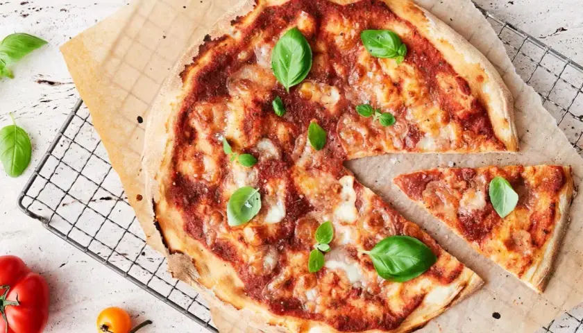 En nybakad pizza med tomatsås, ost och basilika. En bit är bortskuren, perfekt för att njuta av goda pizza kalorier.