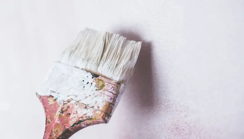 Brocha desgastada con pintura blanca lista para renovar una pared. Se puede pintar encima de pintura de caucho.