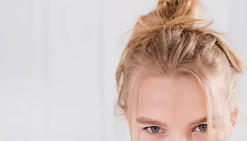 En ung kvinna med kall blond frisyr i en slarvig knut. Hennes gröna ögon möter betraktaren.