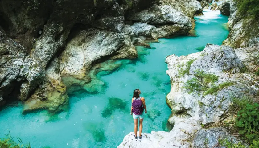 Wanderin am Juliana Trail: Eine Frau mit Rucksack steht auf einem Felsen und blickt auf das türkisfarbene Wasser einer Schlucht.