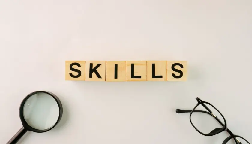 Wooden blocks spell "SKILLS." A magnifying glass and glasses suggest an organization leader carefully assessing talents.