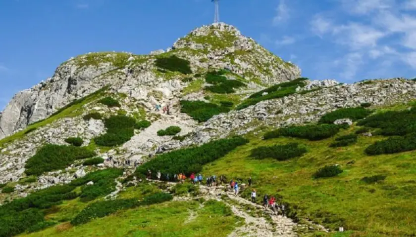 Grupa turystów wspina się kamienistym szlakiem na szczyt Giewontu w Tatrach. Góra przypomina śpiącego rycerza.