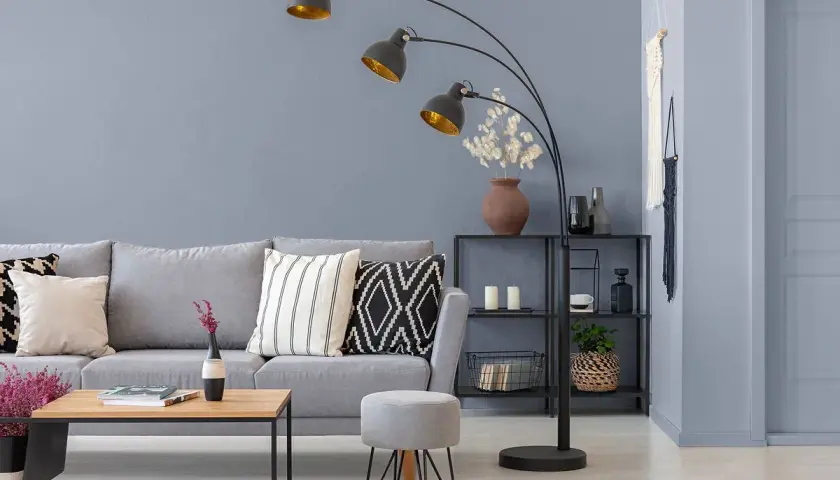 Nowoczesny salon z szarymi ścianami, wygodną sofą i designerską lampą łukową.