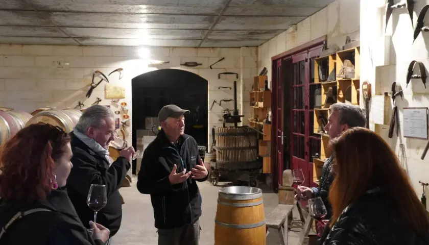 Visite d'une cave à vin du Médoc. Un guide explique la fabrication du vin à des visiteurs, entourés de fûts et d'outils anciens.