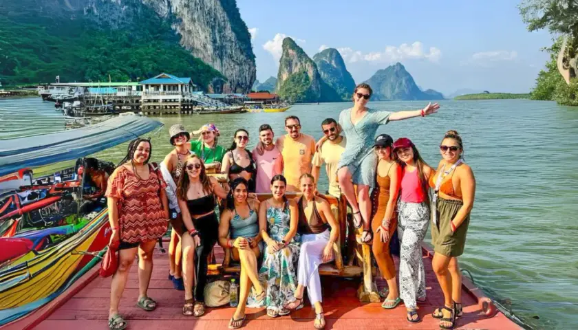 Grupo de amigos disfrutando en un barco en Tailandia, con islas kársticas al fondo. ¡Parece la mejor época para viajar a Tailandia!