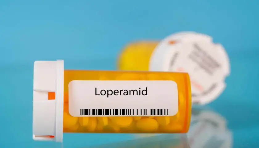 Orange pill bottle with "Loperamid" label and yellow pills inside. Another blurred bottle in the background.