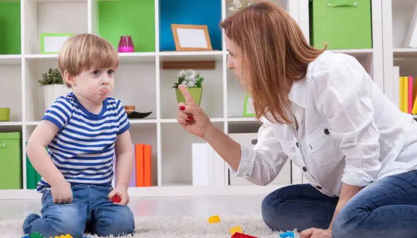 Niño con cara de enfado, actitud negativista desafiante, mientras su madre le regaña.
