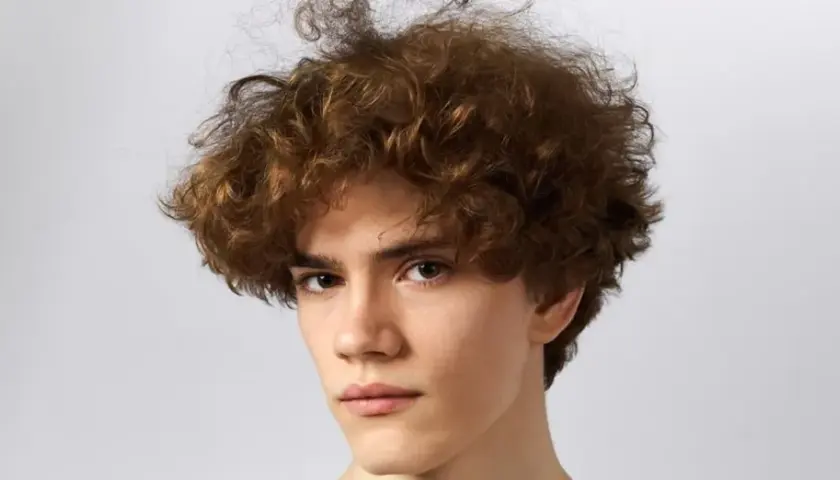 Joven con pelo castaño rizado y voluminoso, un estilo moderno que realza sus rasgos. Cortes pelo rizado hombre.