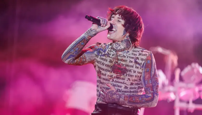 Oli Sykes z Bring Me The Horizon Polska śpiewa na koncercie, ubrany w koszulkę z tatuażami i francuskim tekstem.