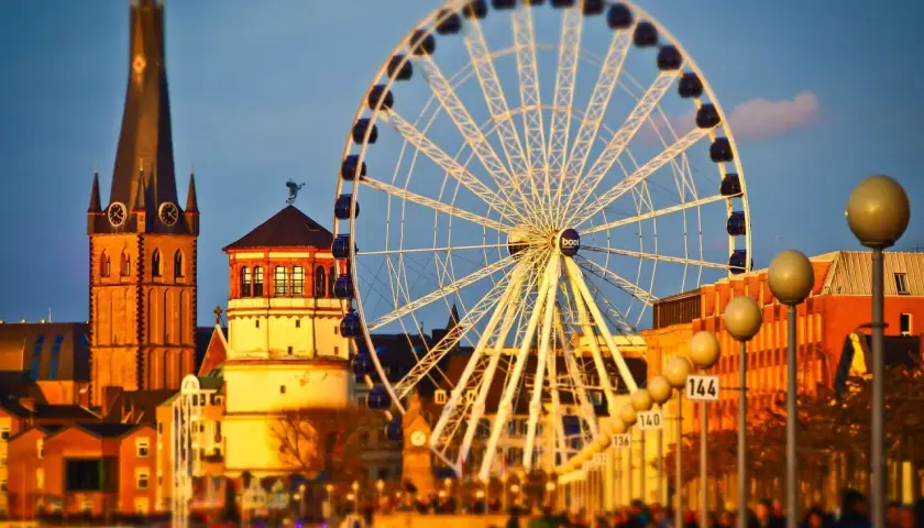 Zachód słońca nad Renem, gdzie dusseldorf atrakcje, takie jak diabelski młyn i wieża kościelna, tworzą malowniczy krajobraz.
