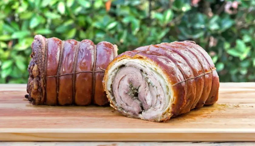 Dwa pieczone kawałki porchetta, zawinięte w skórkę i sznurki, leżą na desce. To pyszne danie, które warto poznać!