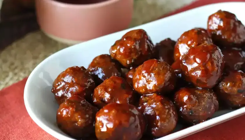 Un plat de boulettes de viande barbecue, brillantes et appétissantes, baignant dans une sauce sucrée. Parfaites pour un apéritif ou un repas convivial.