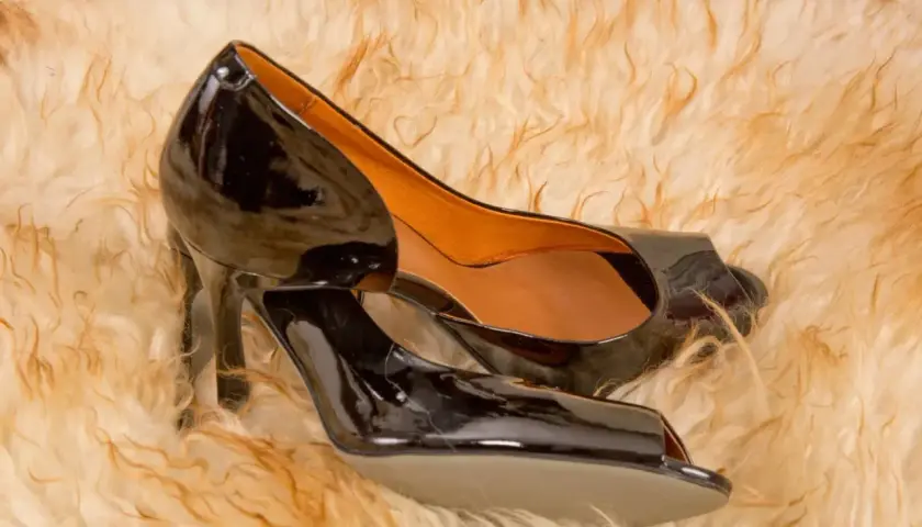 Escarpins noirs en cuir vernis, posés sur un tapis douillet.