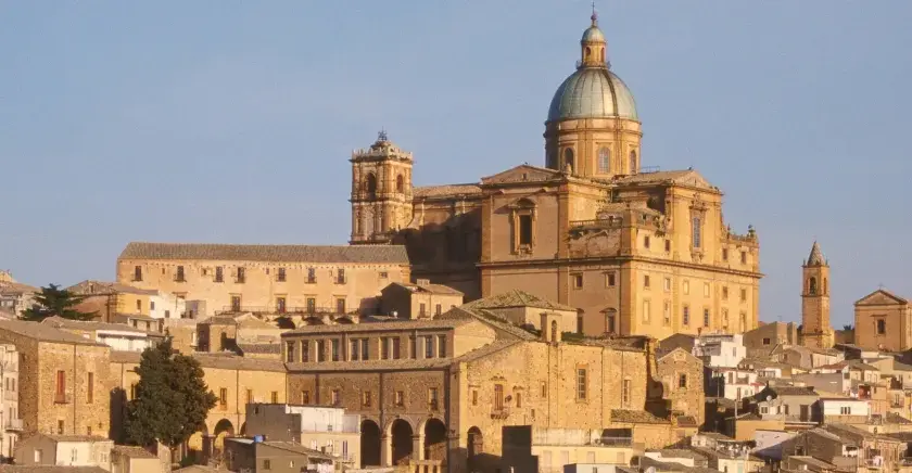 Vue panoramique de la ville de Piazza Armerina en Sicile, dominée par une imposante cathédrale à dôme vert.