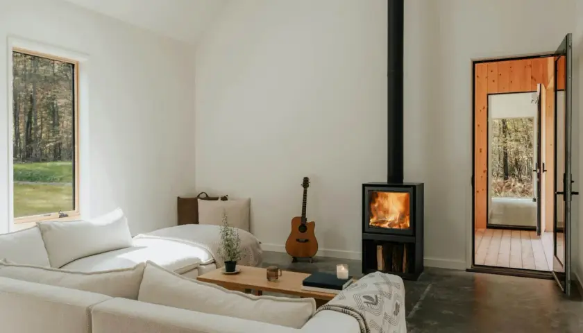 Salon cosy avec poêle à bois allumé, guitare et canapé. Une aide financière pour le tubage de cheminée pourrait rendre ce lieu encore plus chaleureux.