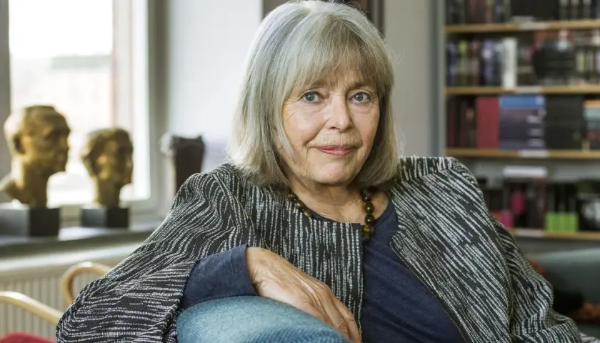 Agneta Pleijel, författare, sitter i en fåtölj med en bokhylla i bakgrunden.
