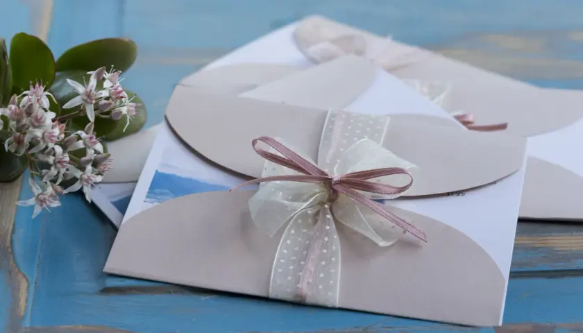 Eleganckie zaproszenia ślubne z kokardkami. Jak odmówić przyjścia na wesele? Delikatne kwiaty dodają uroku.