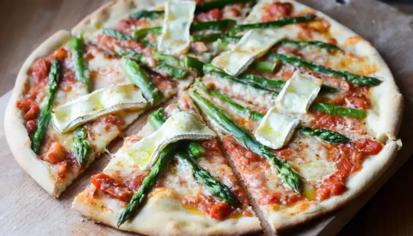Pyszna pizza ze szparagami i serem brie, pokrojona na kawałki, prezentuje się apetycznie na drewnianej desce.