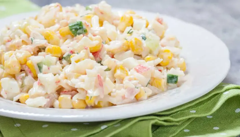 Deliciosa ensalada de arroz con mayonesa, maíz, pepino y surimi, servida en un plato blanco sobre una servilleta verde.