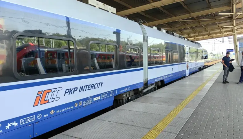 Pociąg PKP Intercity na peronie, z widocznymi odbiciami innych pociągów w oknach.